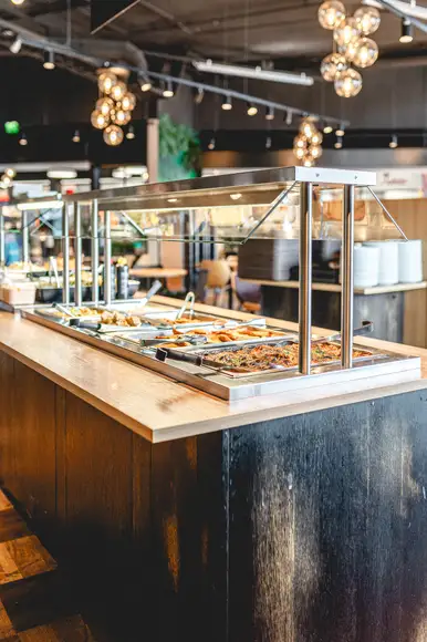 Lähikuva lounasannoksesta, jossa Ståhlbergin omia lihapullia kermakastikkeessa, krutonkeja, slaattia ja perunamuusia. Taustalla lasi kotikaljaa ja lautanen jolla hampurilainen ja ranskalaisia burgerbuffasta.